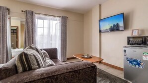 A hotel room with a sofa, a small table, a television, and a minibar.