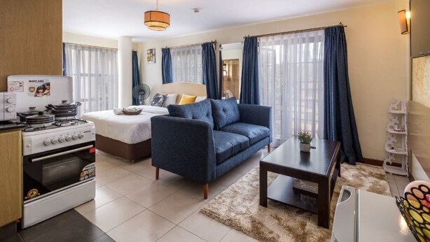 A modern living room with a sofa, a dining table, a kitchen area with a stove, and a large window with curtains.