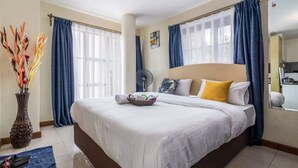 A hotel room with a large bed, a bedside table, a fan, and a window with curtains.