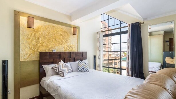 Ein Hotelzimmer mit einem großen Bett, einem Holz-Kopfteil, einer dekorativen Wandverkleidung, einem großen Fenster mit Vorhängen und einem Spiegel.
