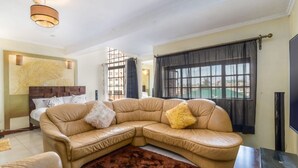 Ein Wohnzimmer mit einem beige-farbenen Ledersofa, einem samtigen Brauntönchen-Teppich und einem Fernseher auf einem Holzständer.