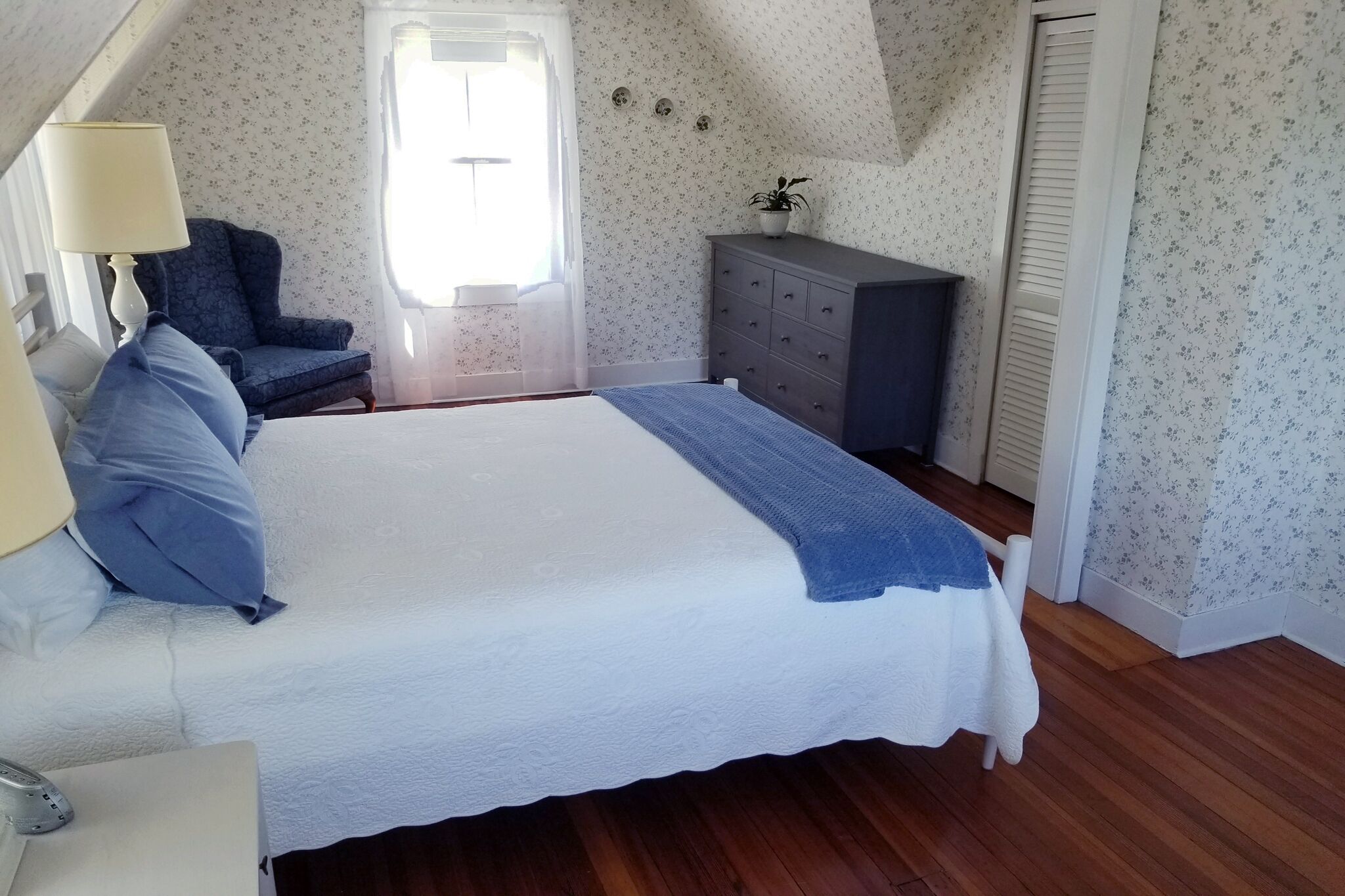 A bedroom with a bed, a chair, a dresser, and a window.
