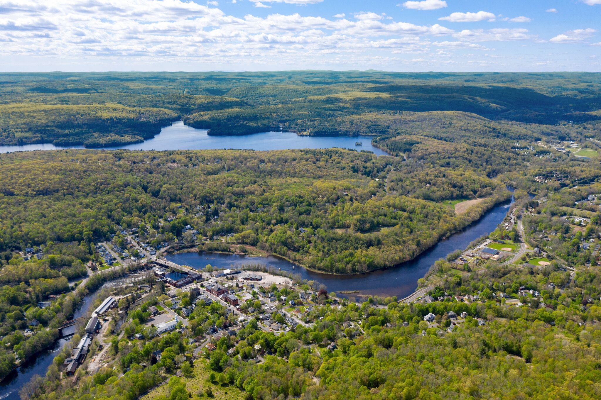 An aerial view of a town with a river, surrounded by dense forests and hills.