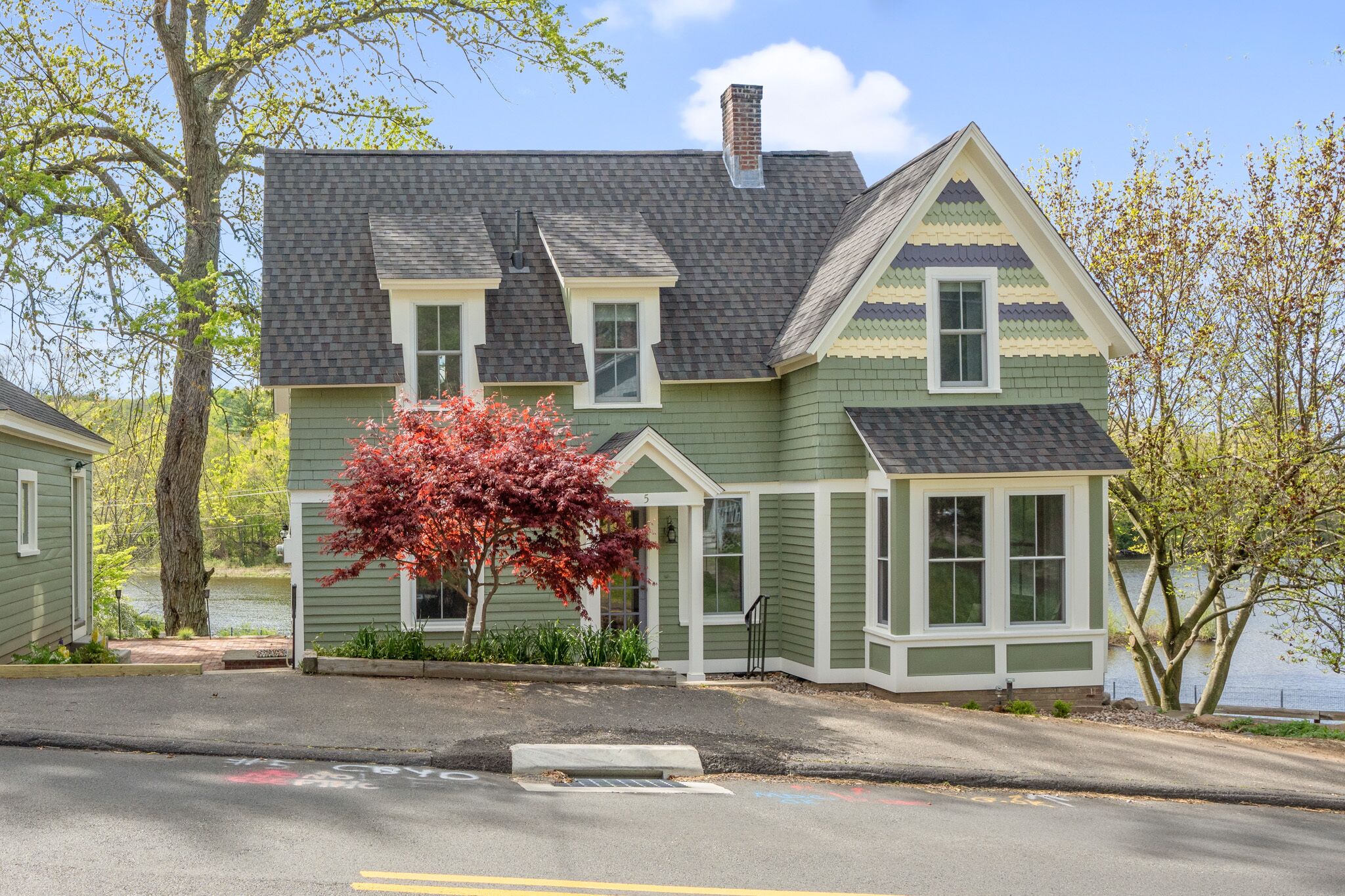 A two-story house with a green exterior and a gray roof, situated near a body of water.