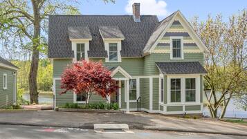 A two-story house with a green exterior and a gray roof, situated near a body of water.