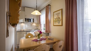 Una cocina compacta con armarios blancos, un microondas y una mesa de comedor con sillas con forma de corazón.