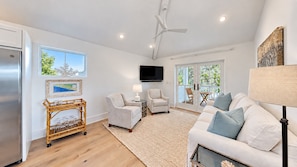 A modern living room with a white sofa, armchairs, a coffee table, a TV, and a balcony with outdoor furniture. - Crystal Blue Persuasion - 1BR/1BA Blue Mountain Beach Carriage House - Sleeps 2 (Santa Rosa Beach)