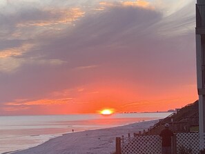 A beach scene with a sunset, a person standing near a fence, and a building in the background. - Crystal Blue Persuasion - 1BR/1BA Blue Mountain Beach Carriage House - Sleeps 2 (Santa Rosa Beach)