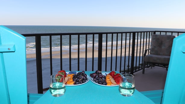 A balcony with a table set for two, overlooking a beach. -  OCEAN BLISS!  Beautiful oceanfront condo with large balcony and amazing views! (North Myrtle Beach)