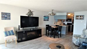 A modern living room with a flat-screen TV, a fireplace, a dining area, and a kitchen in the background. -  OCEAN BLISS!  Beautiful oceanfront condo with large balcony and amazing views! (North Myrtle Beach)