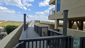 A wooden boardwalk leading to a building with a balcony, a sign about pet waste, and a view of the beach. -  OCEAN BLISS!  Beautiful oceanfront condo with large balcony and amazing views! (North Myrtle Beach)