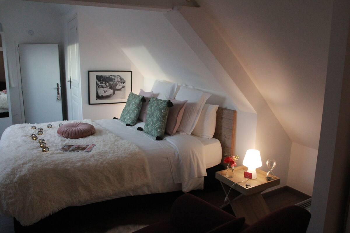 A bedroom with a bed, pillows, a bedside table with a lamp, and a framed picture on the wall.