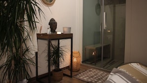Een knus ingerichte kamer met een glazen deur naar een balkon, een tafeltje met een kaars en een bloempot.