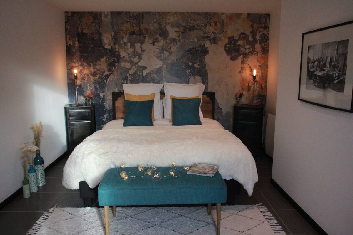 A bedroom with a large bed, two bedside tables, a bench, a textured wall, and a framed picture on the wall.