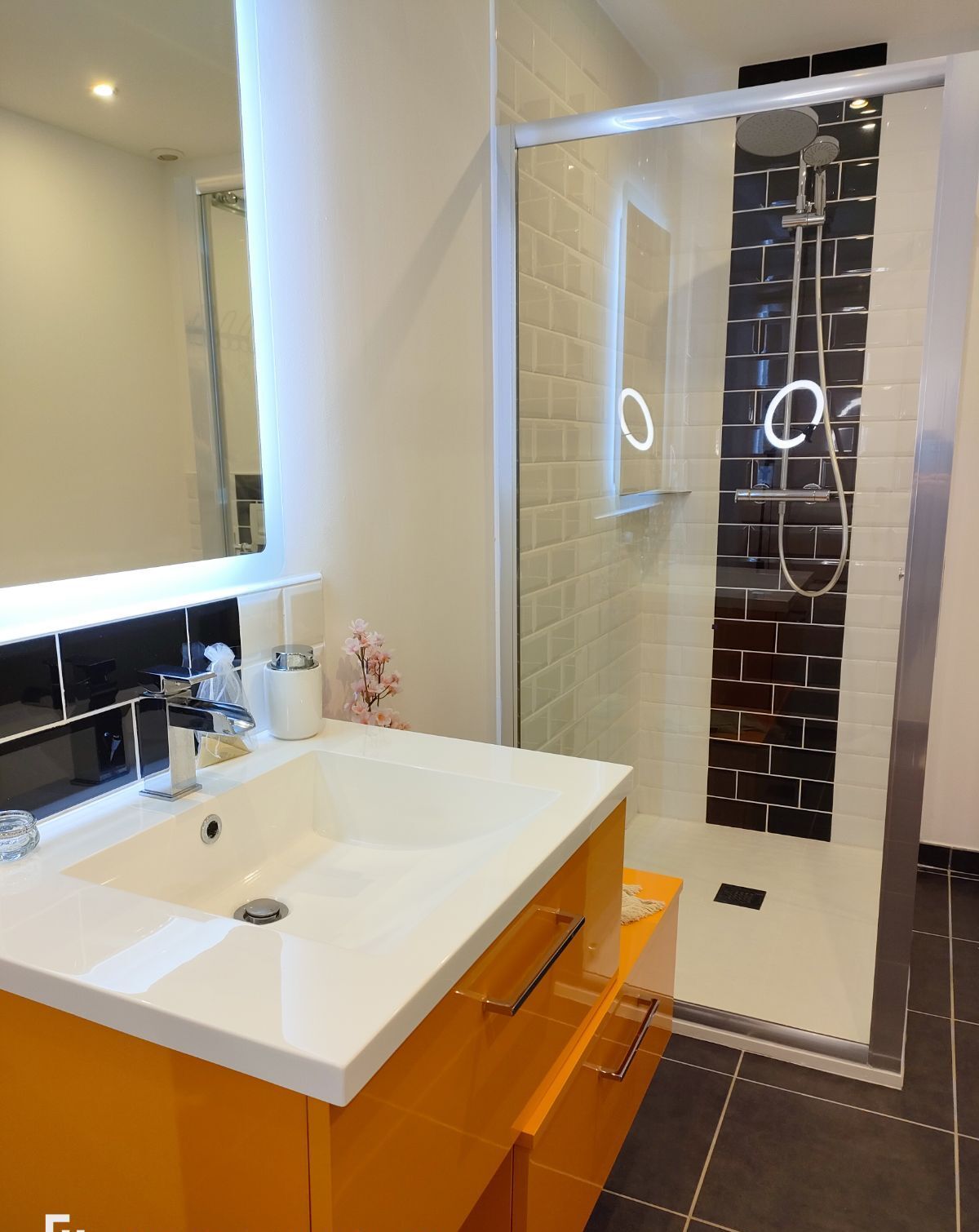 Ein modernes Badezimmer mit einem weißen Waschbecken, einer Duschkabine aus Glas und einem Spiegel über dem Waschbecken.
