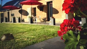 Een gebouw met modern design, herkenbaar aan een plat dak en grote ramen. Op het gazon staan rode parasols en een lantaarn, en rode bloemen op de voorgrond.