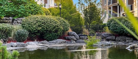 A residential area with a pond, greenery, and multi-story buildings.