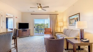 Ein Hotelzimmer mit Flachbildfernseher, einer Sitzecke, einem Esstisch, einer Lampe und einem Balkon mit Blick.