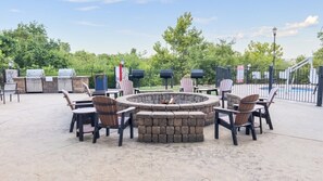 An outdoor patio with a circular fire pit, seating area, and a pool in the background.