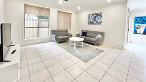 A spacious living room with a grey sofa, a white coffee table, and a TV on a stand. - Our most popular home. Your family and staff will love it here! Bed & bath linen hire included. Unlimited NBN WIFI internet. Airconditioning throughout. Easy Parking. Spacious and relaxing. (Richmond)