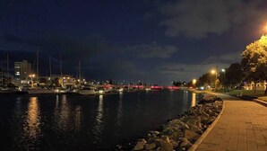 A nighttime marina with boats docked, a paved walkway, and city buildings in the background. - Our most popular home. Your family and staff will love it here! Bed & bath linen hire included. Unlimited NBN WIFI internet. Airconditioning throughout. Easy Parking. Spacious and relaxing. (Richmond)