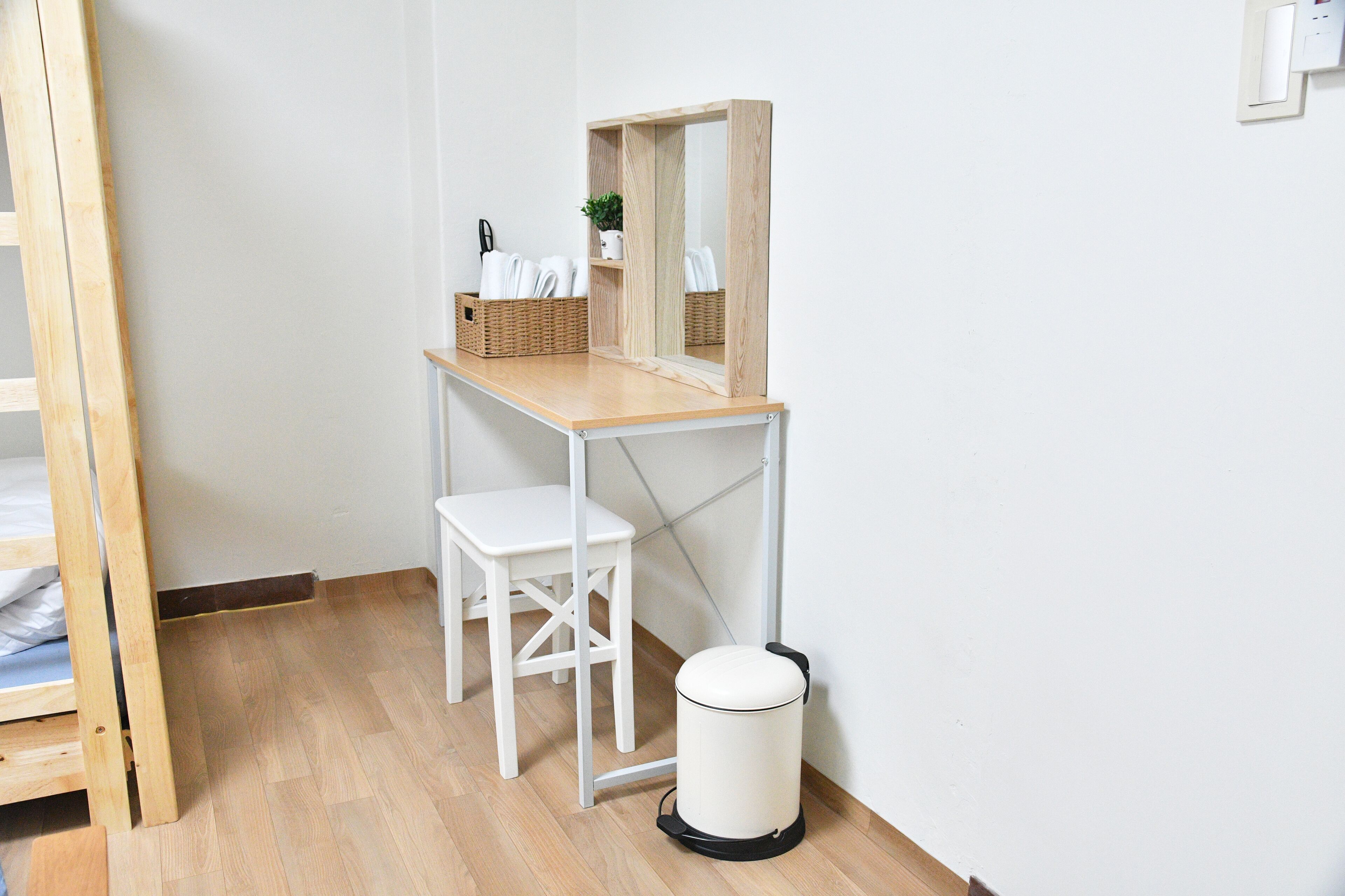 Ett litet, rent rum med ett skrivbord i trä, en vit stol och en papperskorg.