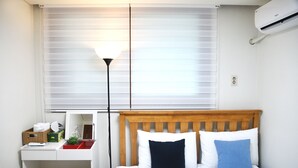 Ein Schlafzimmer mit Bett, Nachttisch, Lampe und Jalousien.