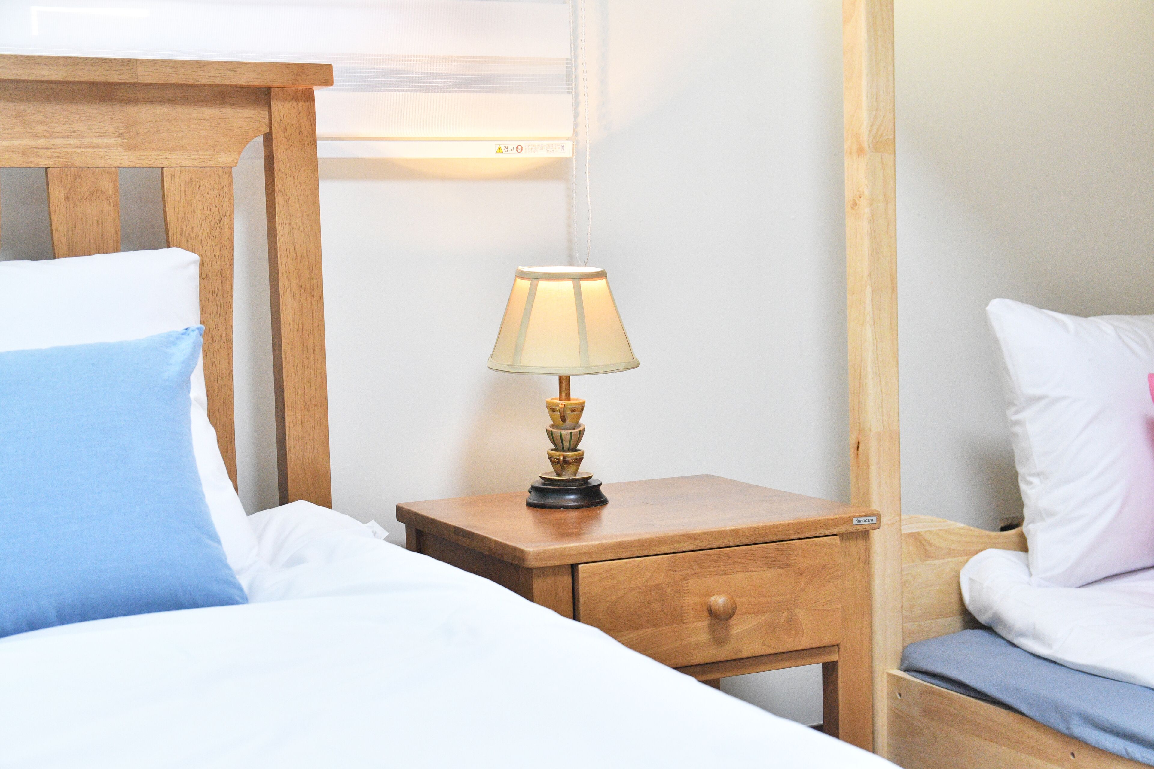 Una cama bien hecha con almohadas blancas y azules, una mesita de noche de madera con una lámpara y un cajón pequeño.