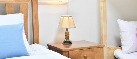 Una cama bien hecha con almohadas blancas y azules, una mesita de noche de madera con una lámpara y un cajón pequeño.