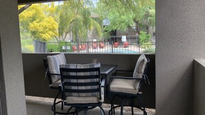 Un patio techado con mesa y sillas, vista a una piscina y un área exterior cercada con sillas rojas.
