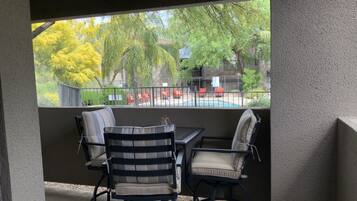 Un patio couvert avec une table et des chaises, une vue sur une piscine et un espace extérieur clos avec des chaises rouges.