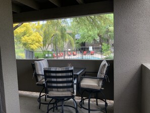 A covered patio with a table and chairs, a view of a swimming pool, and a fenced outdoor area with red chairs. - Vacation Near Sabino Canyon and Ventana Canyon Resort - Bikes Included! (Tucson)