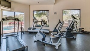 Un gimnasio con cintas de correr, elípticas y una piscina visibles a través de las ventanas.