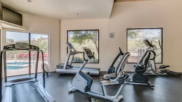 Une salle de sport équipée de tapis de course, de vélos elliptiques et d’une piscine visible à travers les fenêtres.