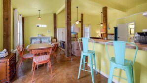 Une cuisine avec des poutres en bois, un coin repas avec des chaises en métal et un bar avec des tabourets.