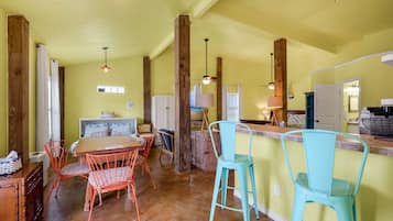A kitchen with wooden beams, a dining area with metal chairs, and a bar area with stools.