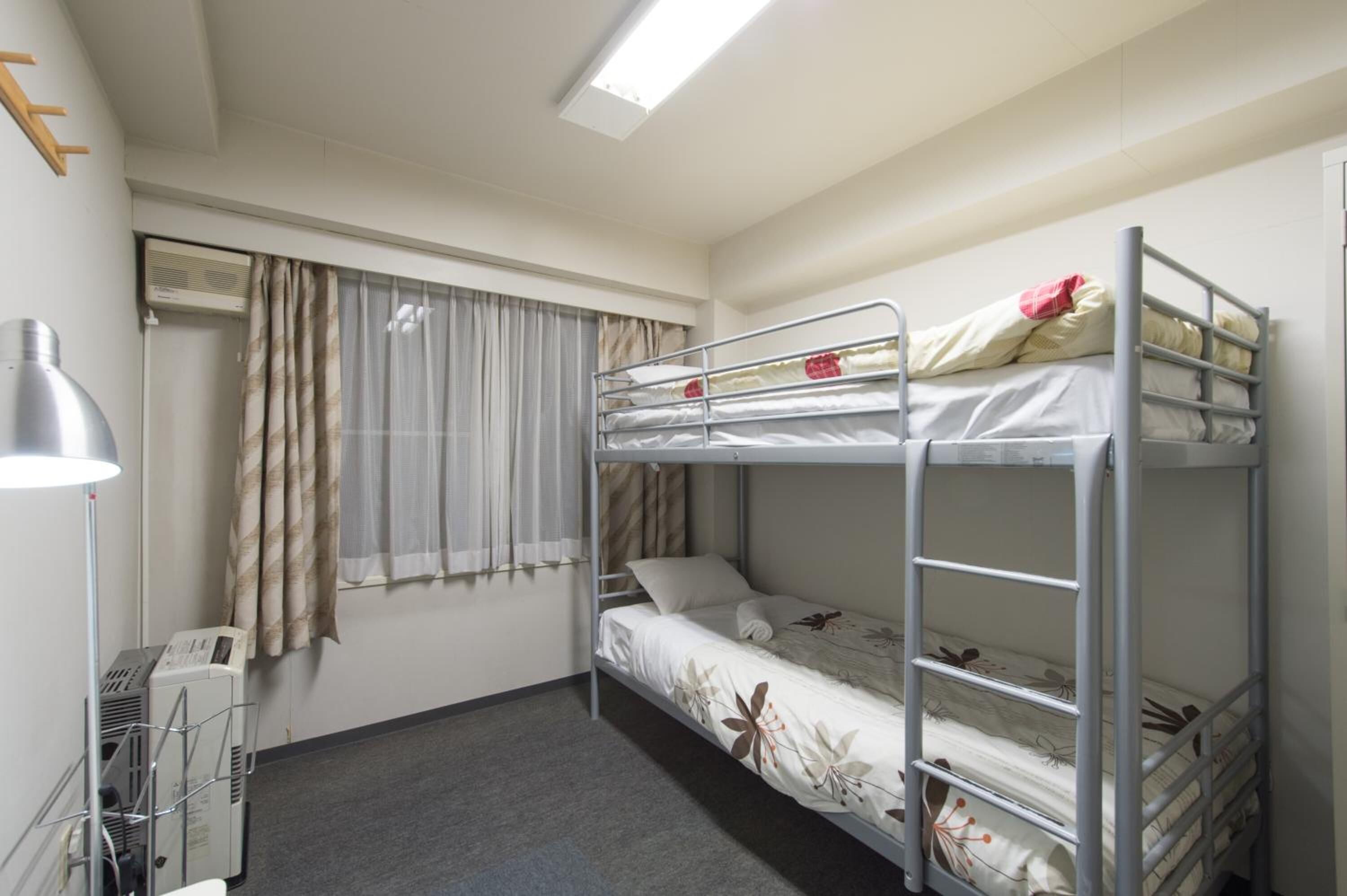 Une chambre avec un lit superposé, un ventilateur de plafond, un appareil de climatisation et une fenêtre avec des rideaux.