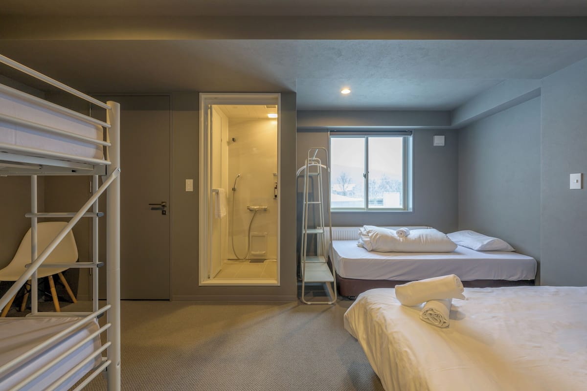 A hotel room with a bunk bed, a walk-in shower, a window, and a neatly made bed.
