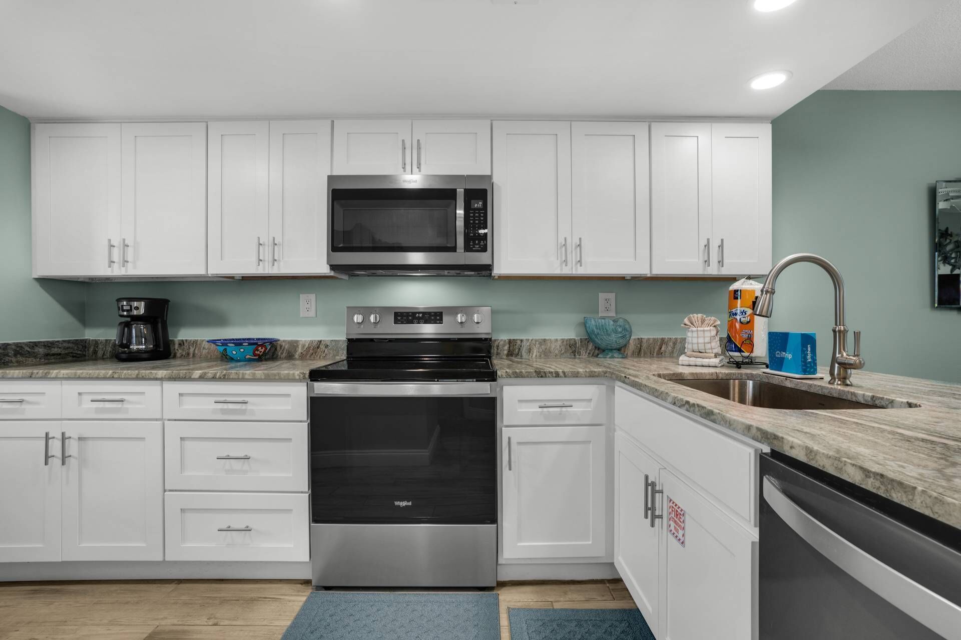 A modern kitchen with white cabinets, stainless steel appliances, a granite countertop, and a blue rug.