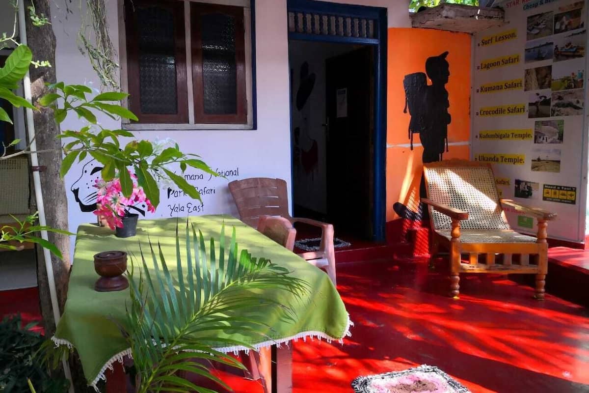 Una habitación con piso rojo, una mesa con mantel verde, una silla y un cartel en la pared.