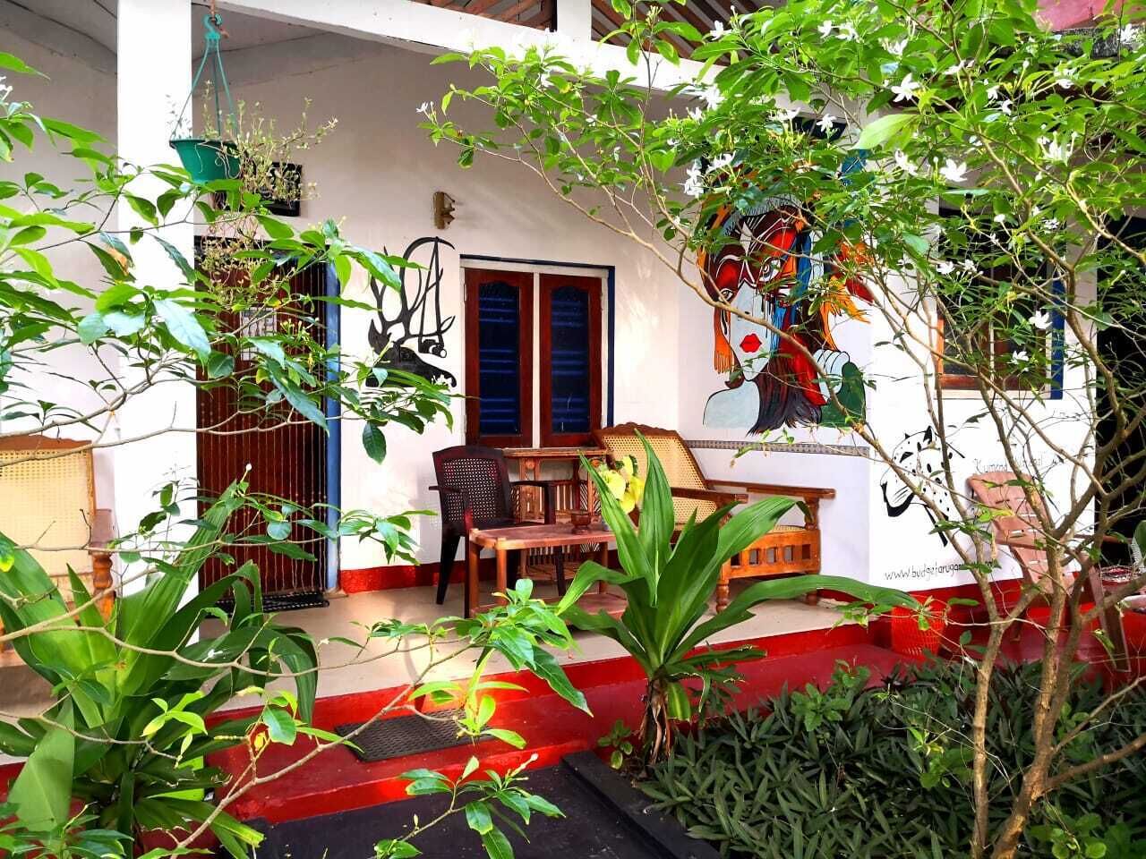 A covered outdoor seating area with a table and chairs, surrounded by lush greenery and a colorful mural on the wall.