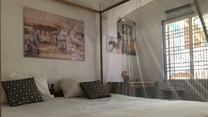 Een slaapkamer met een bed, gestreept kussen, klamboe en een muur met een groot schilderij.