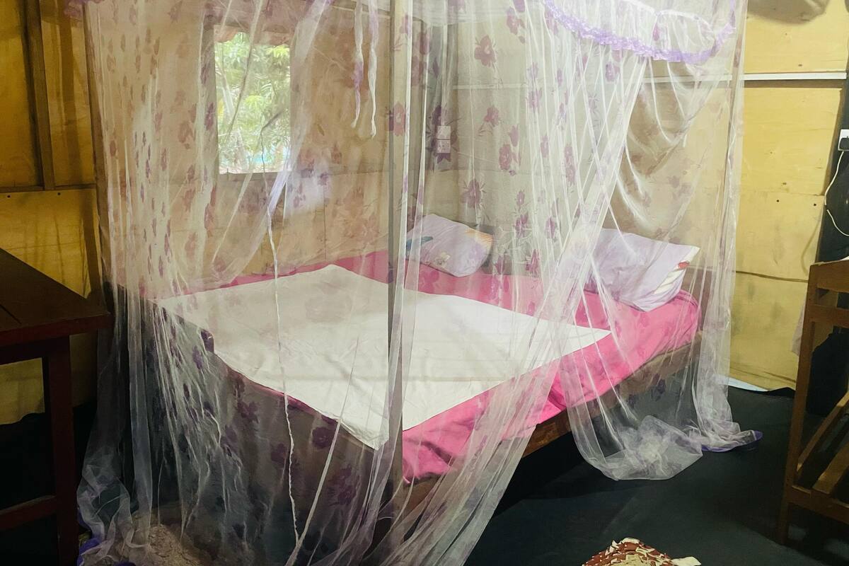 Ein Bett mit Moskitonetz, einem Holzkopfstück und einem Fenster mit Blick auf Grünflächen.