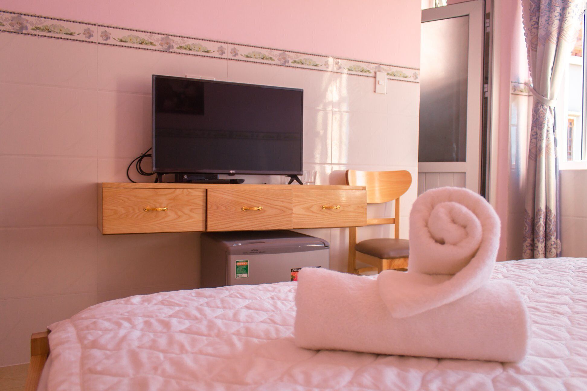 Habitación de hotel con una cama, un televisor sobre una cómoda de madera, un escritorio pequeño y una toalla enrollada sobre la cama.