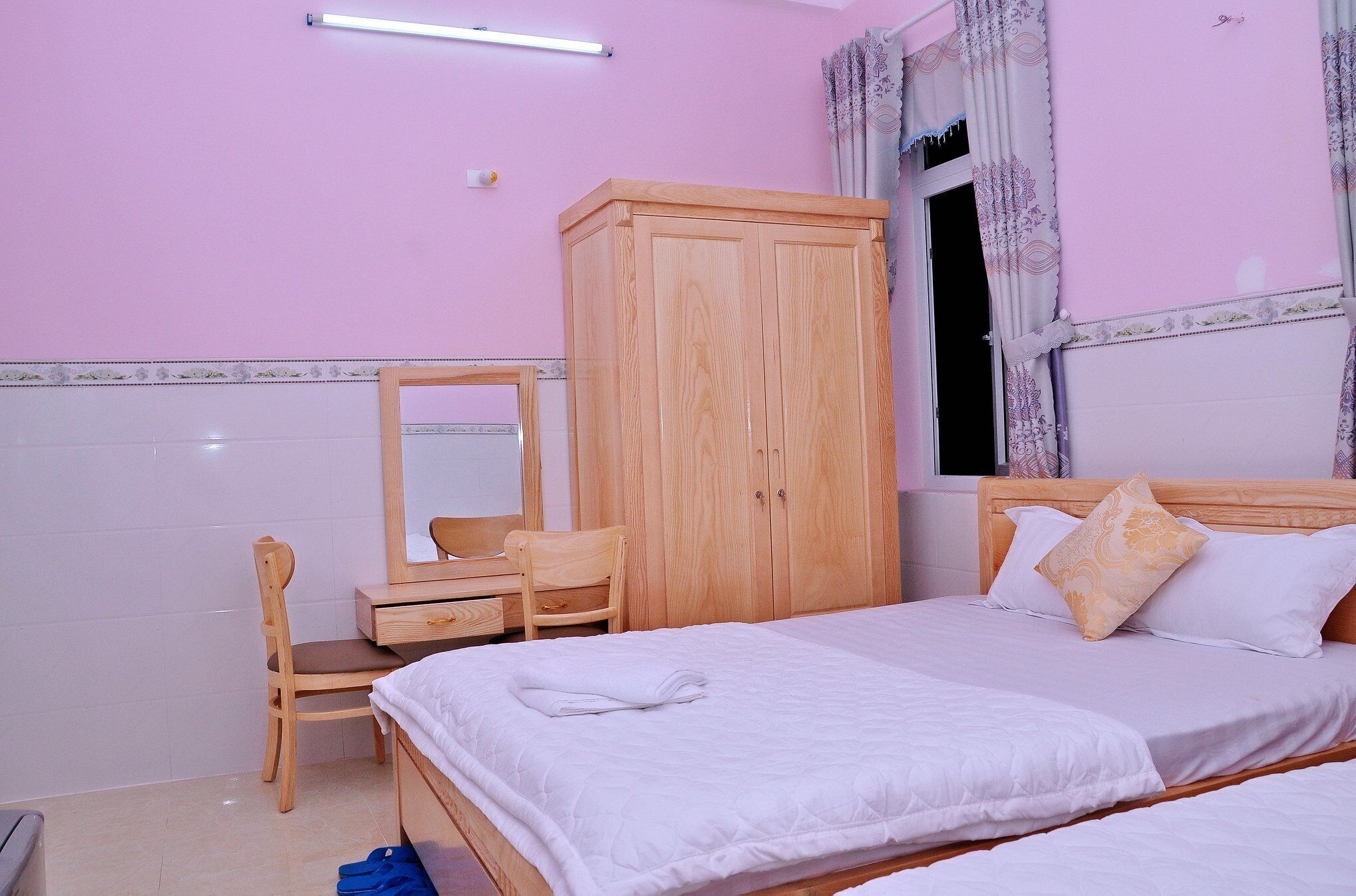 A bedroom with a bed, a wooden wardrobe, a desk with a chair, and a mirror.