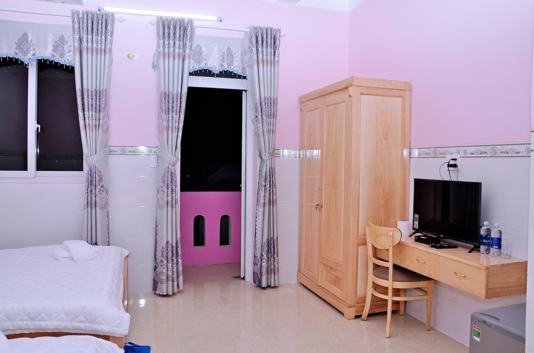 A hotel room with a bed, a desk with a computer, a TV, and a wardrobe.