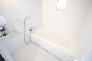 A small, white bathroom with a bathtub, a shower, and a mirror. - Tommy Condominium Wakasa (Naha)