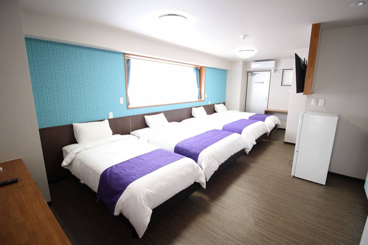 A hotel room with three beds, a TV, a desk, and a window with curtains.