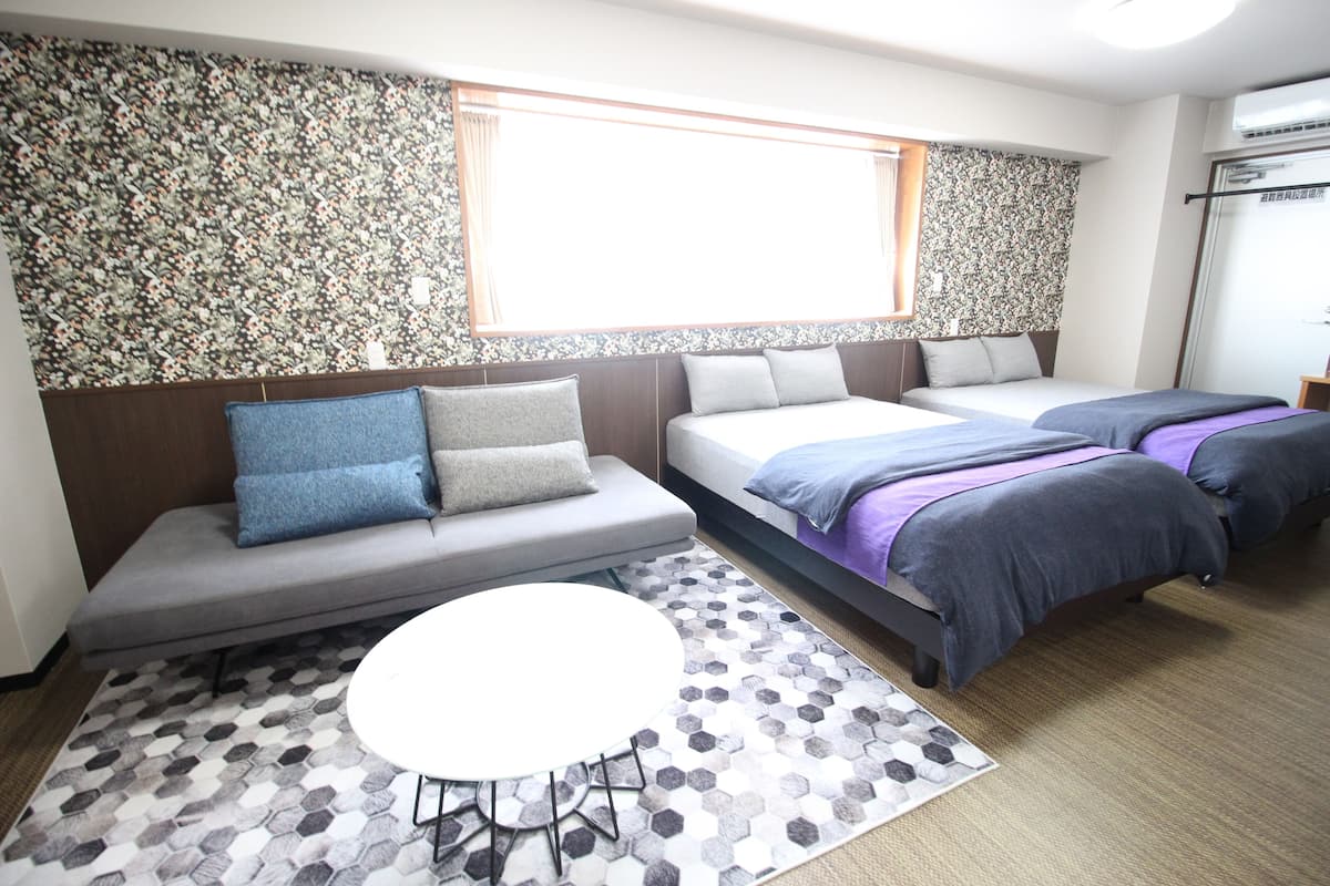A hotel room with a sofa, two single beds, a small round table, and a patterned rug.