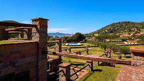 An outdoor area with stone structures, a pool, and a view of a hillside with houses. - Appartamento Via Dei Lecci - APPARTAMENTO I LECCI (Rio nell'Elba)